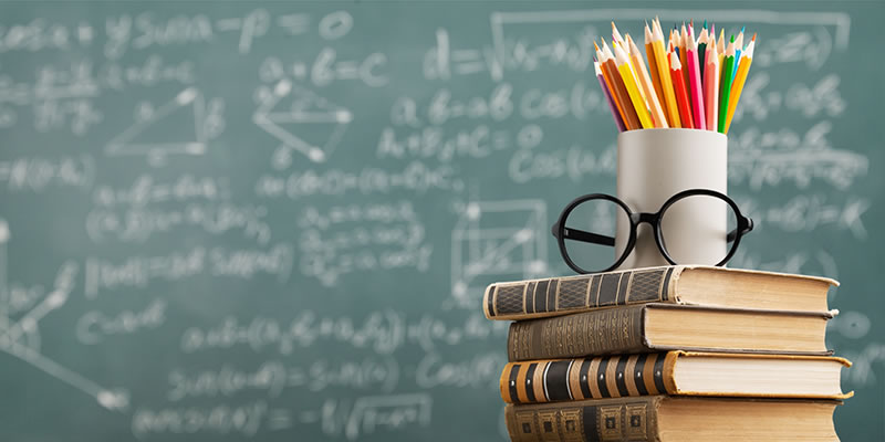 Stack of books and pencils in front of a blackboard 