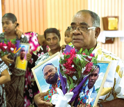 A man carrying flowers and pictures of deceased loved ones.
