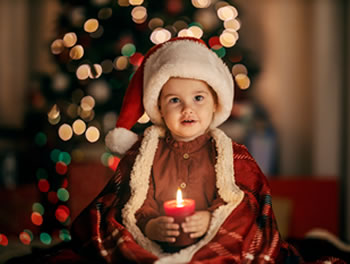 A child in a Christmas hat and robe holding a candle