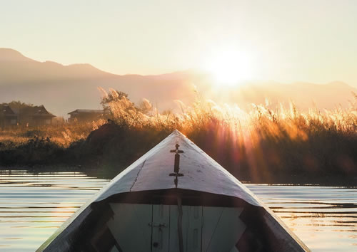 Canoe on a lake pointing toward the rising sunn