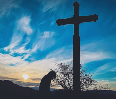 Person kneeling before a cross outdoors.