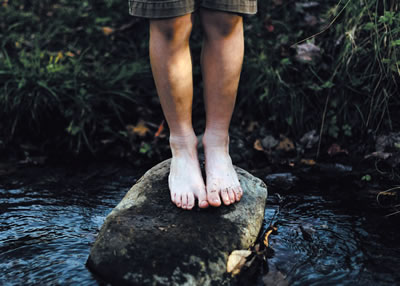 A child's bare feet standing on a rock in a stream