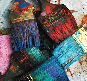 Colorful used paint brushes sitting on a table.