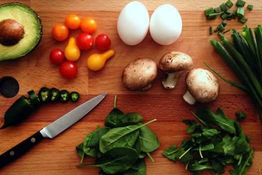 Avacado, onions, tomatos, eggs, mushrooms and leafy greens on a cutting board
