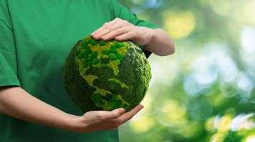 A person holds a green globe of the earth
