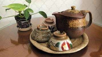 A table with a potted plant and a tray with a teapot and three small cups