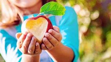 A child holds out an apple with a heart carved out of it.