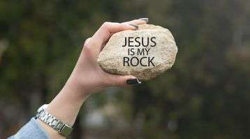 A hand holding a rock with the words Jesus Is My Rock