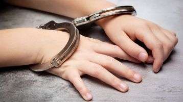 A childs hands in handcuffs rest on a table.