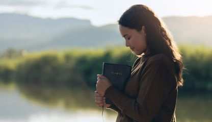 A young women near a lake holding a bible in reflection and thanks.