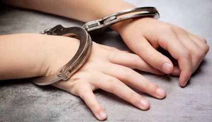 A childs hands in handcuffs rest on a table.