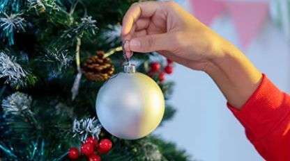 A hand hanging an ornament on a Christmas tree