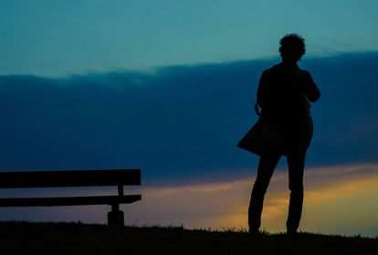 Solitary person standing on a hillside near a park bench