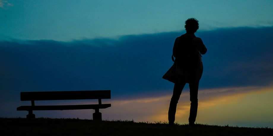 Solitary person standing on a hillside near a park bench