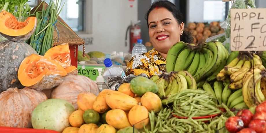 Woman looks smiling from behind her counter at a market in Fiji