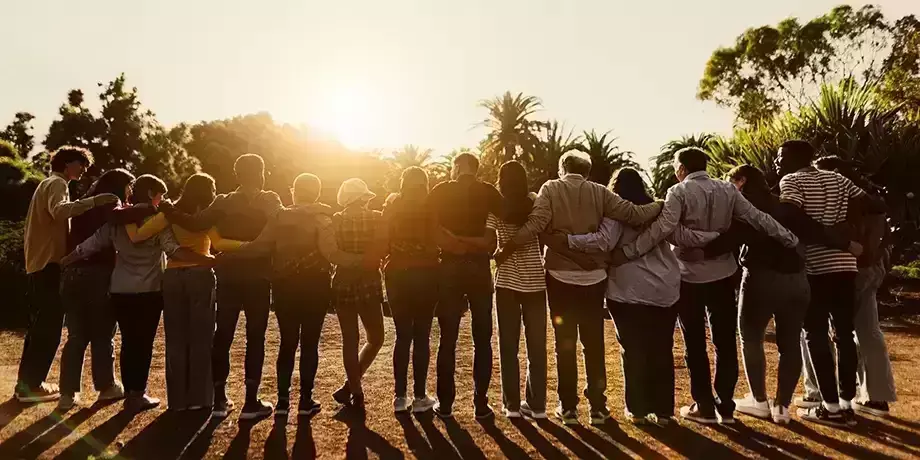 A group of people with arms interlocked facing the rising sun