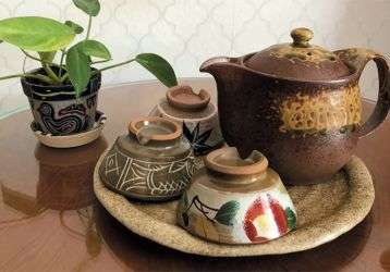 A table with a potted plant and a tray with a teapot and three small cups
