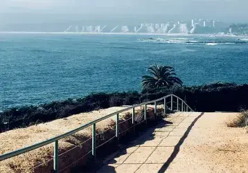 Walkway overlooking a shoreline with buildings in the distance.