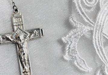A silver crucifix of a rosary setting on white lace