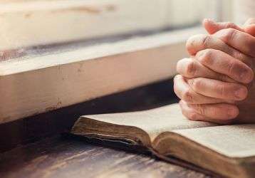 Hands clasped in prayer on a bible.